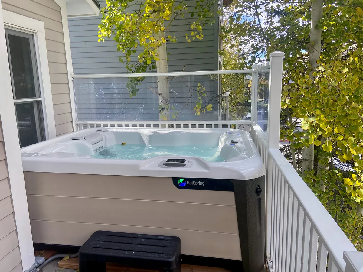 An inviting hot tub sits on the deck, surrounded by lush foliage and a generous deck area for lounging or socializing. The setup suggests both morning serenity and lively evening gatherings under the open sky.