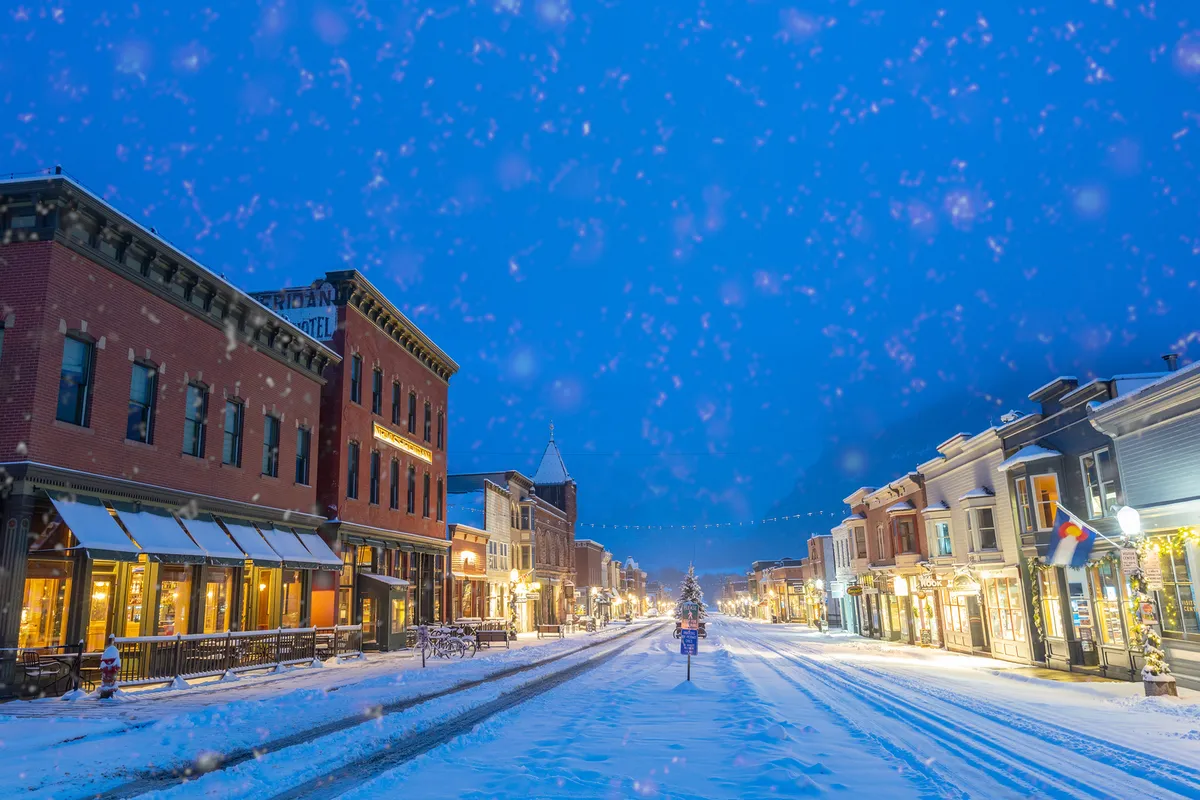 A cozy winter main street scene with historic buildings, snow-covered streets, and decorated trees. The inviting ambiance suggests opportunities for walks, shopping, and enjoying festive local culture just steps away.