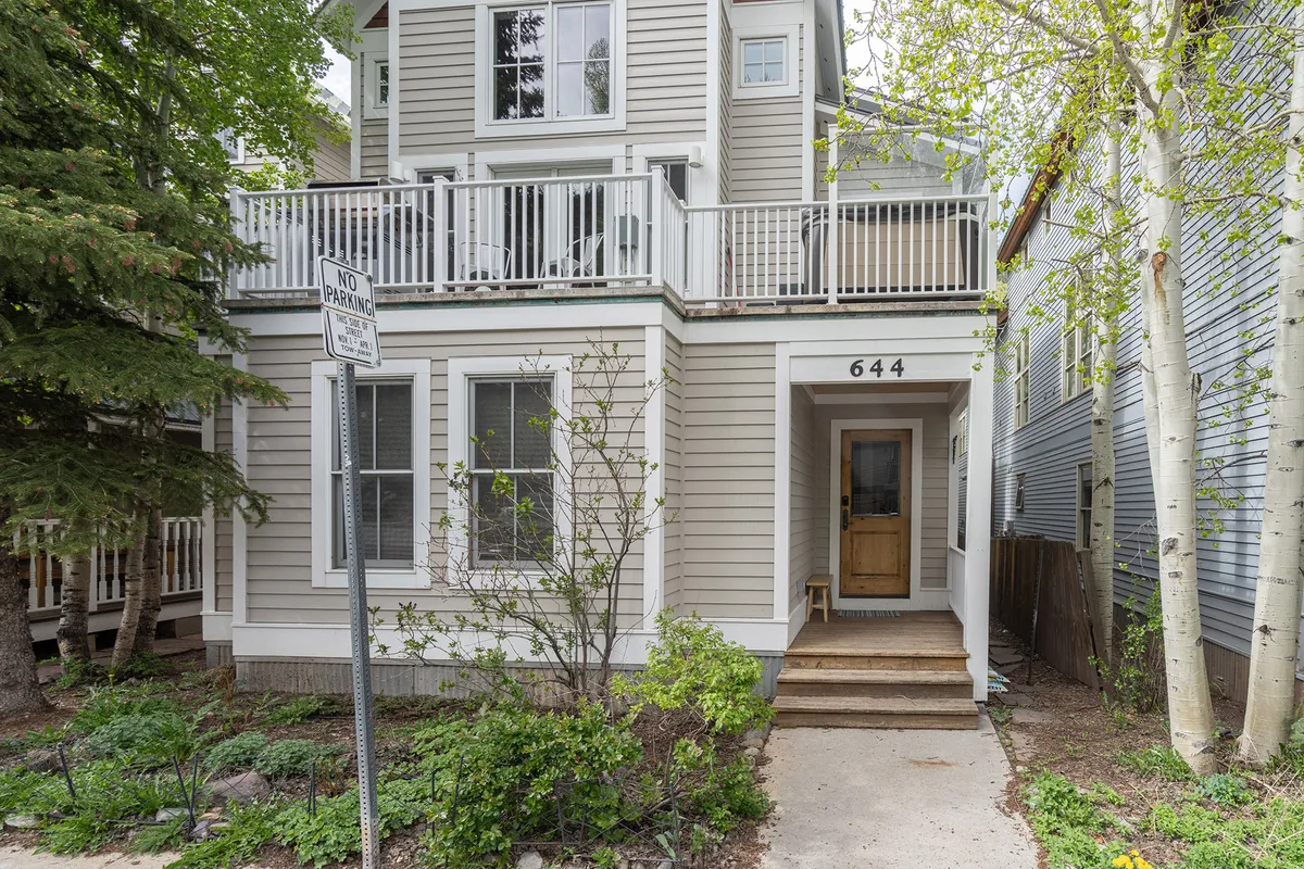 A welcoming exterior shot featuring the home's front entrance, balcony, and surrounding greenery. The scene suggests a space ideal for gathering outdoors, socializing, or enjoying morning coffee and sunset views with friends.