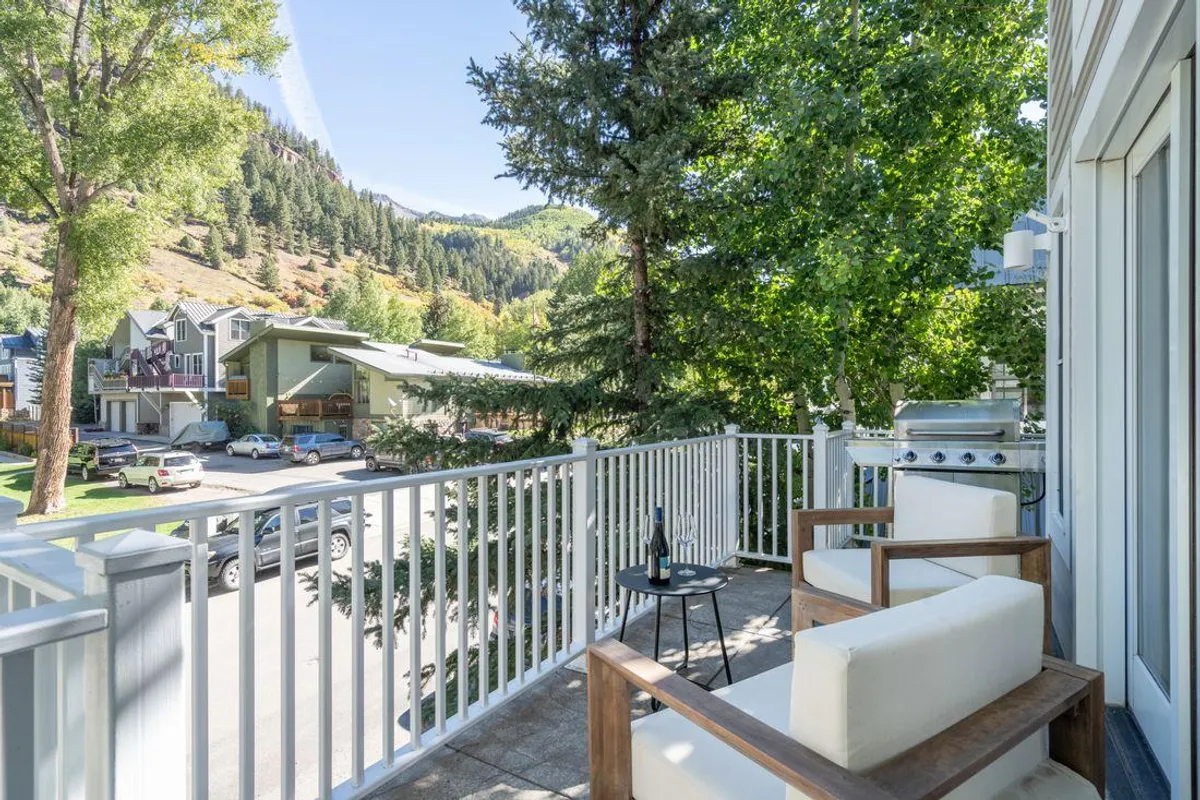An exterior balcony scene with comfortable seating, lush greenery, and a stunning mountain view. The mood is tranquil and inviting, ideal for morning coffee or sunset gatherings.