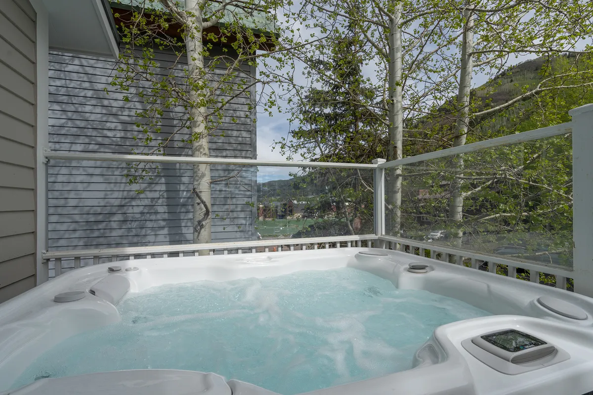 A tranquil outdoor hot tub nestled among trees, with views of the surrounding landscape. The setting exudes relaxation and togetherness, perfect for unwinding after a day exploring festivals, town parks, or local shops with the family.