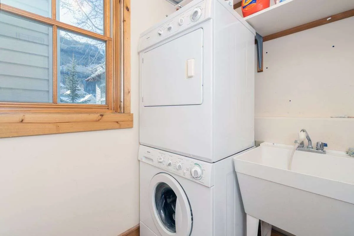 A bright and practical laundry room featuring a stacked washer and dryer, utility sink, and a window that lets in natural light, emphasizing convenience for handling daily chores and family needs.