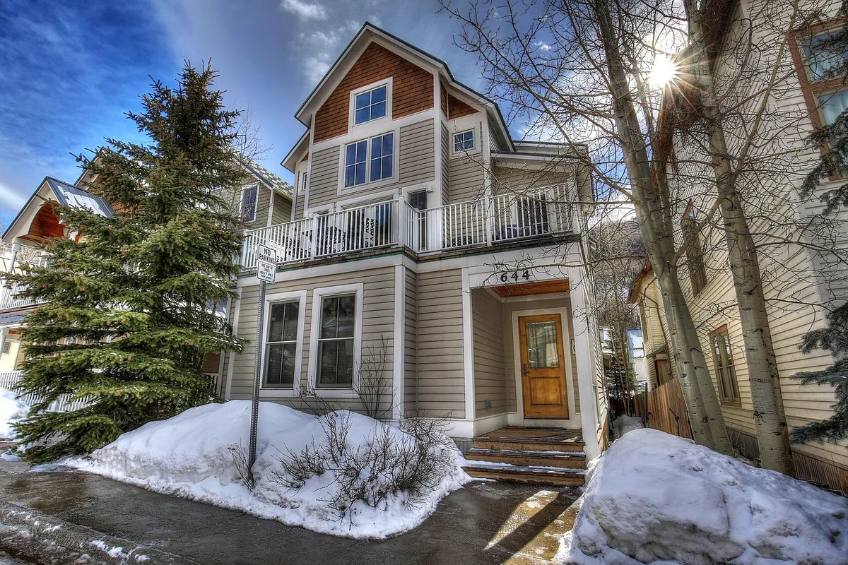 A warm, welcoming home exterior with a front porch, large windows, and a snow-covered landscape. The balcony and views reinforce the connection between indoor comfort and the inspiring outdoor scenery.