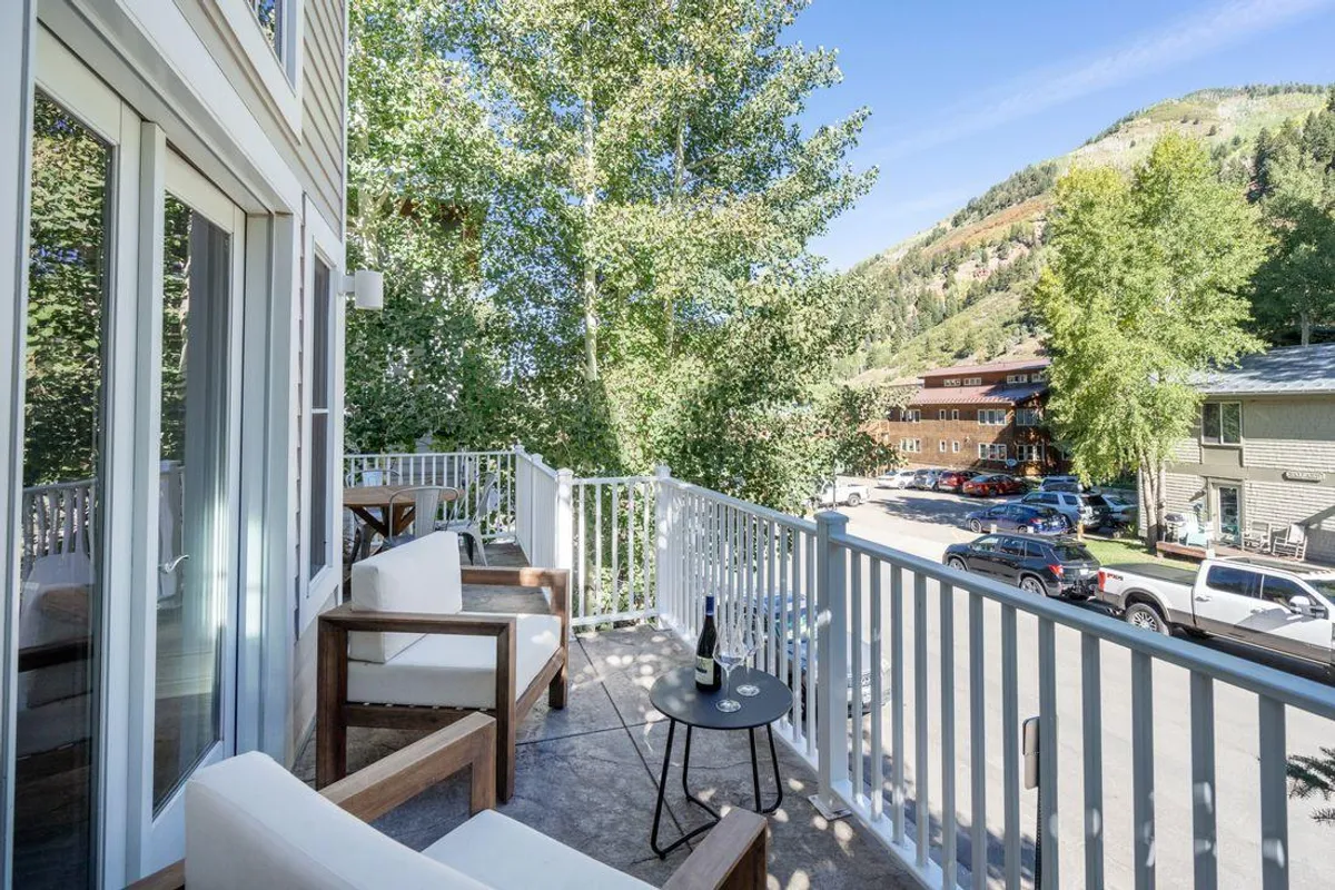 A scenic balcony setup with seating and a table adorned with wine, surrounded by lush greenery and mountain views. This outdoor space is ideal for relaxing, socializing, and enjoying nature after exploring the town, hinting at both adventure and comfort.