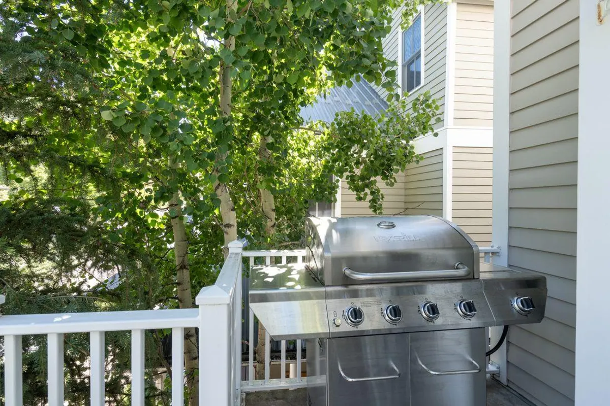 An outdoor setting with a grill surrounded by lush greenery, indicating a space for barbecuing, outdoor dining, and relaxed gatherings. The casual atmosphere hints at memorable evenings shared with loved ones under the open sky.