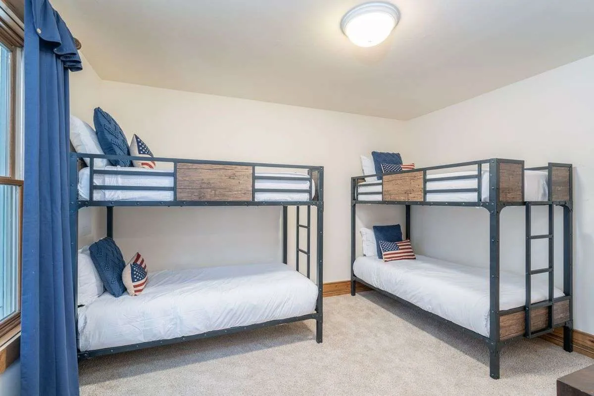 A playful bedroom with bunk beds, decorative pillows, and a window with curtains. The space feels cheerful and relaxed, clearly tailored for kids or groups of friends, offering a sense of fun and togetherness.