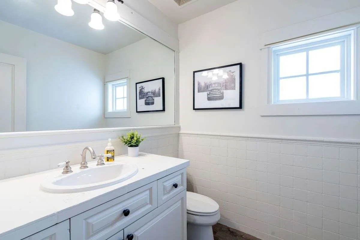 A bright bathroom featuring a vanity sink, framed photographs, and natural light streaming through a window. The mood is calm and inviting, suggesting an ideal space for personal grooming and a refreshing start to the day.