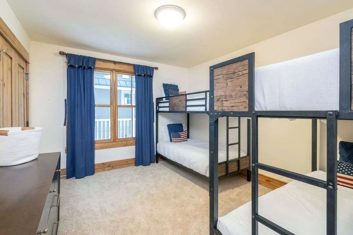 A cozy bedroom with sturdy wooden bunk beds, a sunlit window, and a dresser, suggesting a welcoming space for children or siblings to sleep, play, and create memories together.